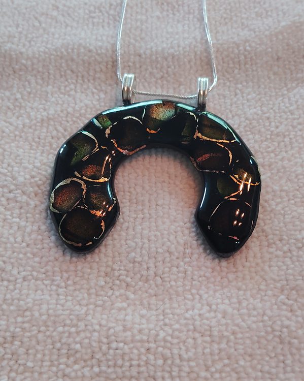 Black horseshoe-shaped glass pendant with bronze and green pebble shapes, two silver bails