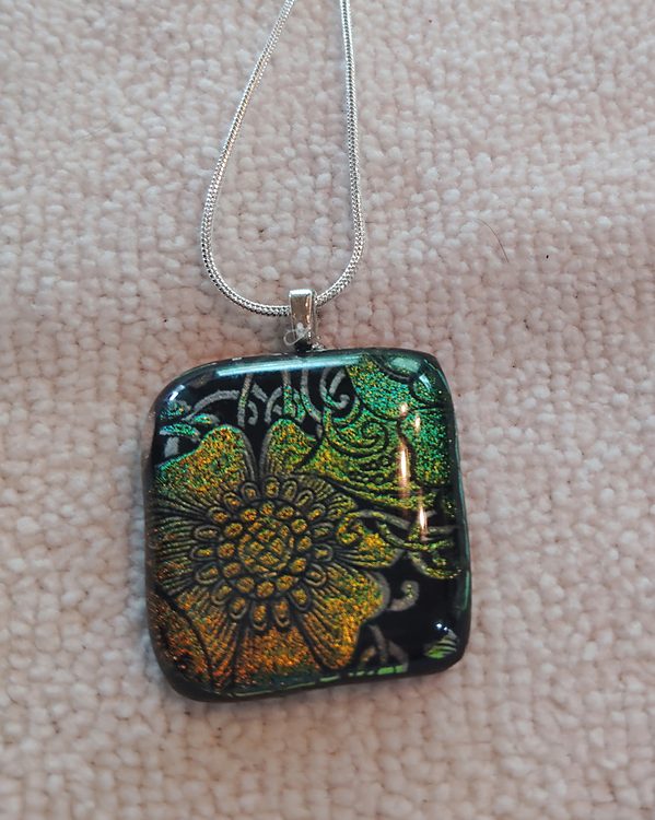 Square glass pendant with an etched gold and green flower pattern on black, silver snake chain