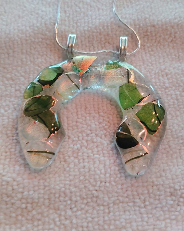 Clear horseshoe-shaped glass pendant with green leaf pieces fused inside, two silver bails