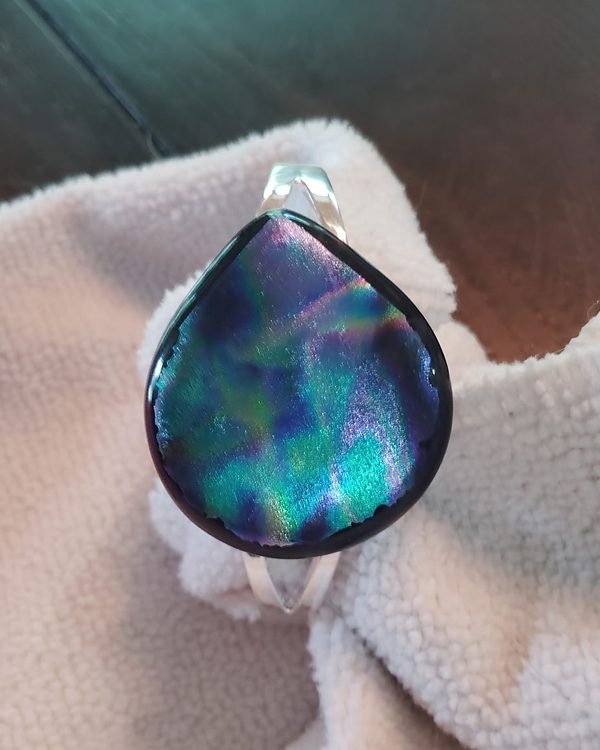 Silver cuff bracelet set with a teardrop of purple, teal and green glass